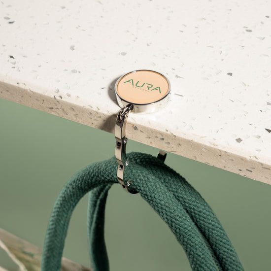 AURA Bag Hanger hook in use, holding bag handles from a table edge