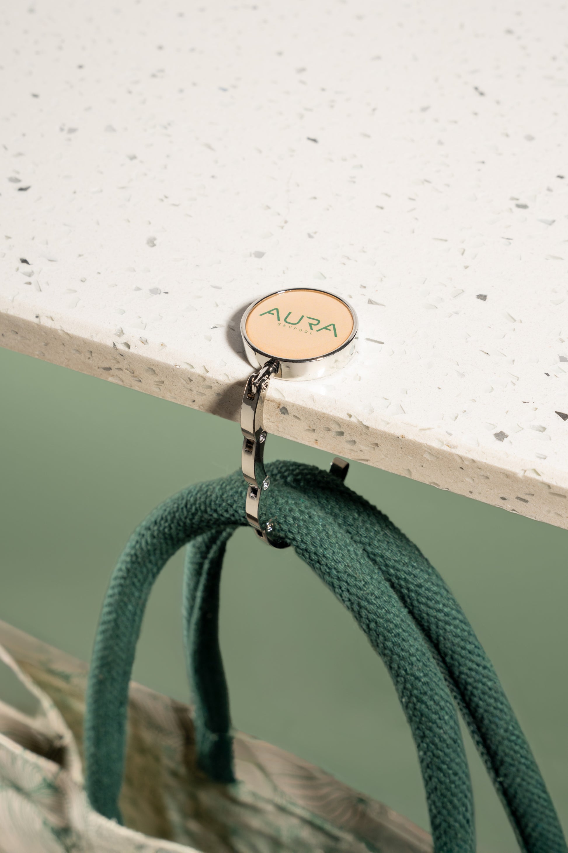 AURA Bag Hanger hook in use, holding bag handles from a table edge