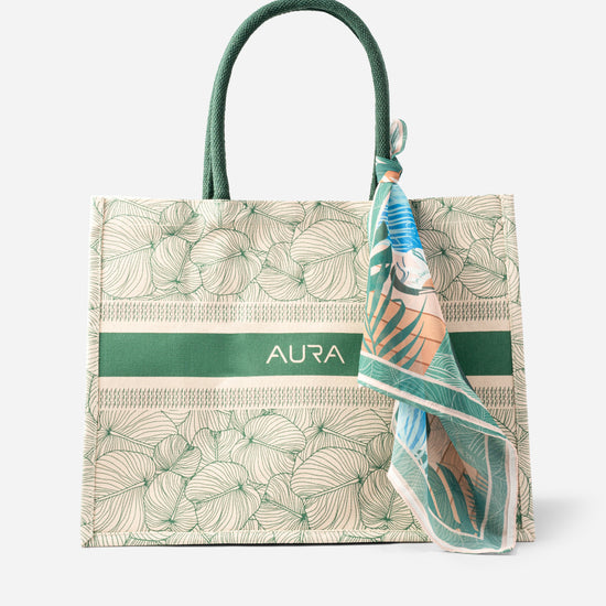 Front view of AURA Signature Tote Bag with green leaf print, green woven handles and AURA logo stripe