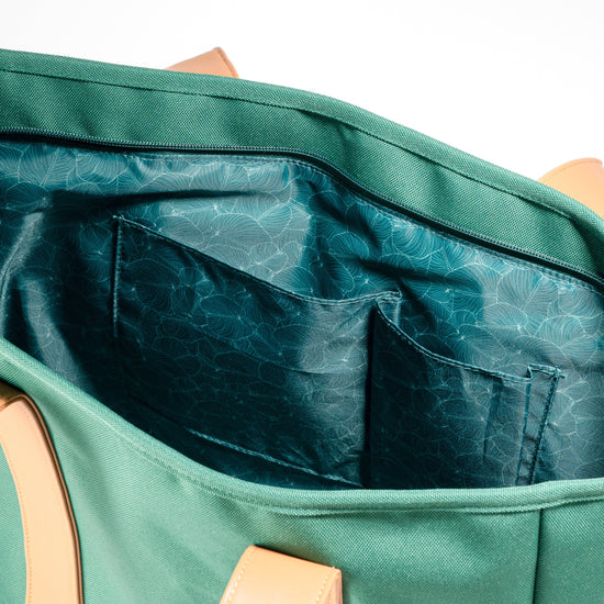 Open interior of AURA Beach Bag Palm Green showing teal leaf-print lining and slip pockets
