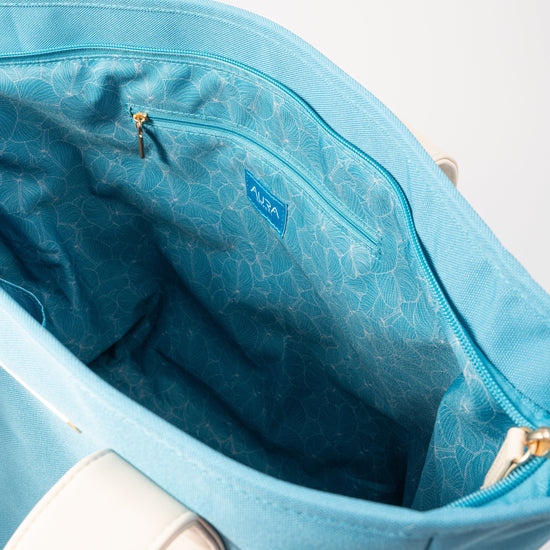 Open interior of AURA Beach Bag Whisper Blue showing teal leaf-print lining and zip pocket