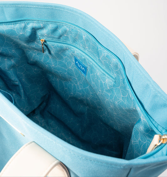 Open interior of AURA Beach Bag Whisper Blue showing teal leaf-print lining and zip pocket