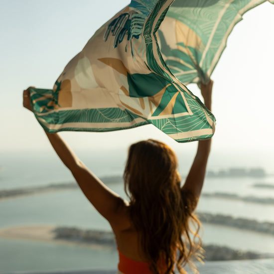 AURA Dubai Skyline Silk Scarf in Green, held aloft against the Palm Jumeirah skyline