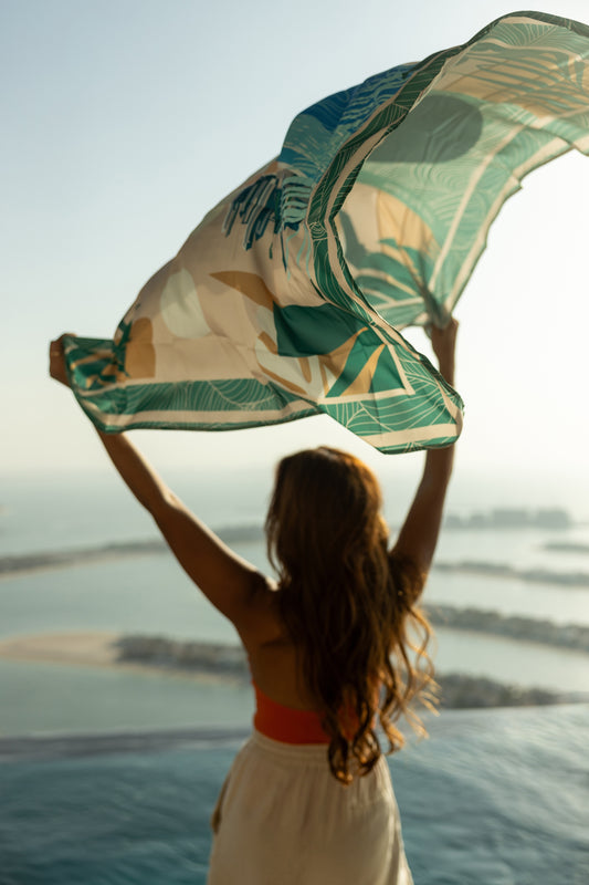 AURA Dubai Skyline Silk Scarf in Green, held aloft against the Palm Jumeirah skyline