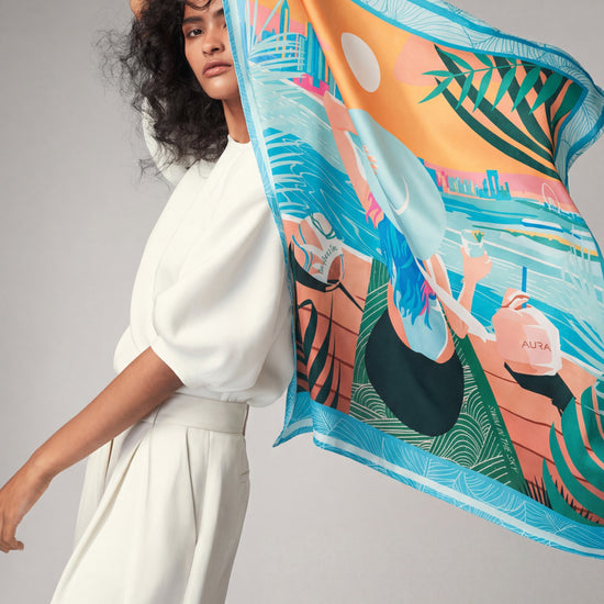 AURA Dubai Skyline Silk Scarf in Sky Blue, held up by a model against a studio backdrop
