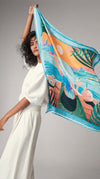 AURA Dubai Skyline Silk Scarf in Sky Blue, held up by a model against a studio backdrop