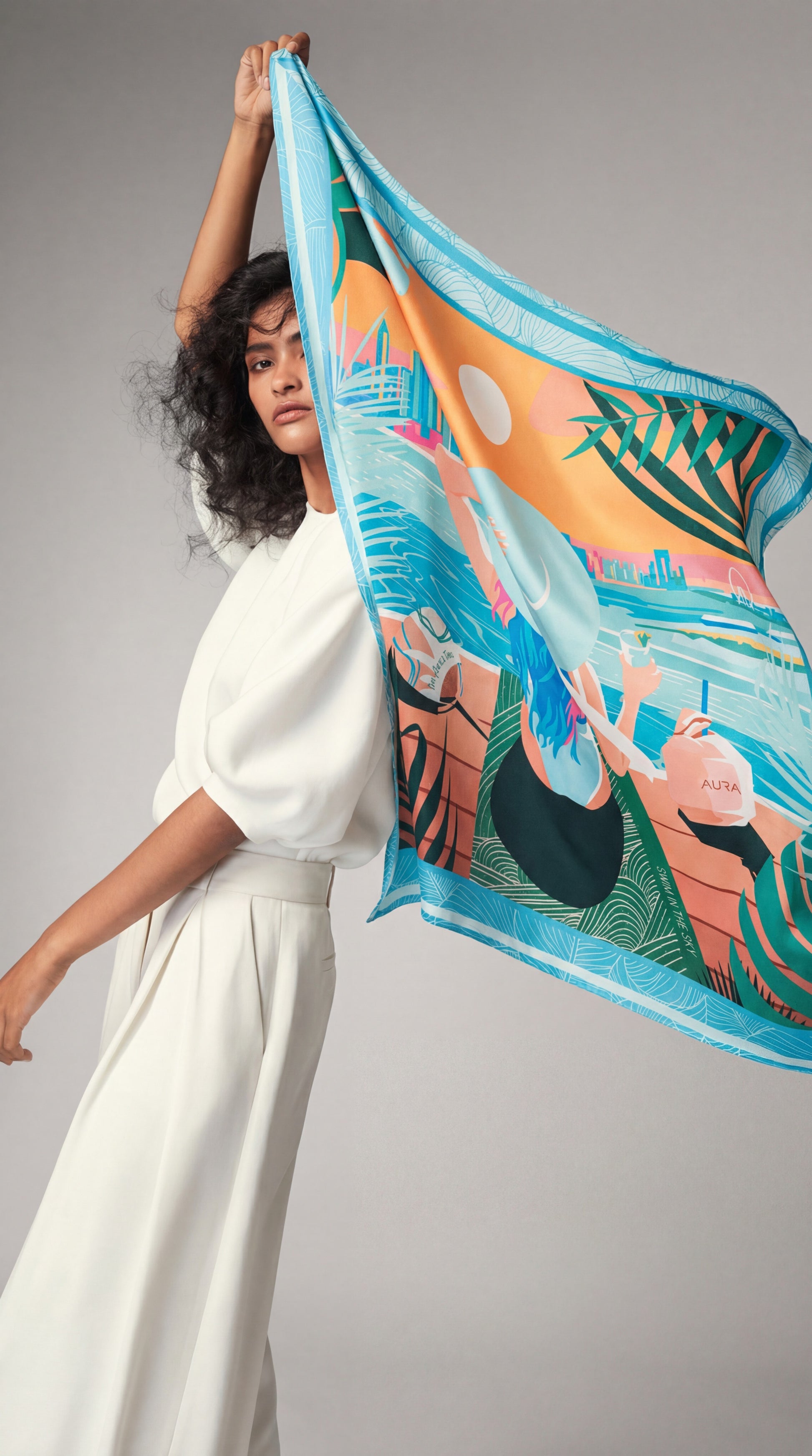 AURA Dubai Skyline Silk Scarf in Sky Blue, held up by a model against a studio backdrop