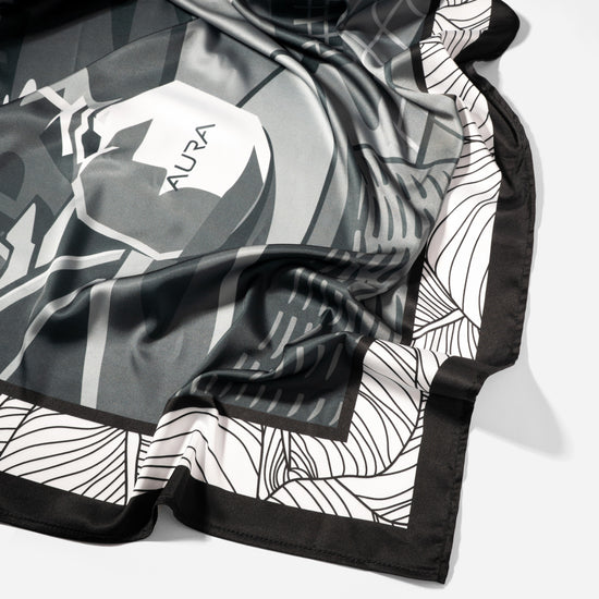 Monochrome Skyline Silk Scarf, draped close-up showing the AURA label and border print