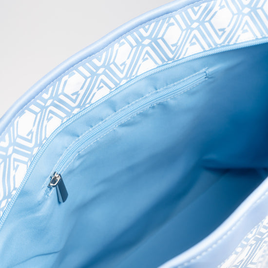 Open interior of The Monogram Bag Azure Blue showing sky-blue satin lining and zip pocket