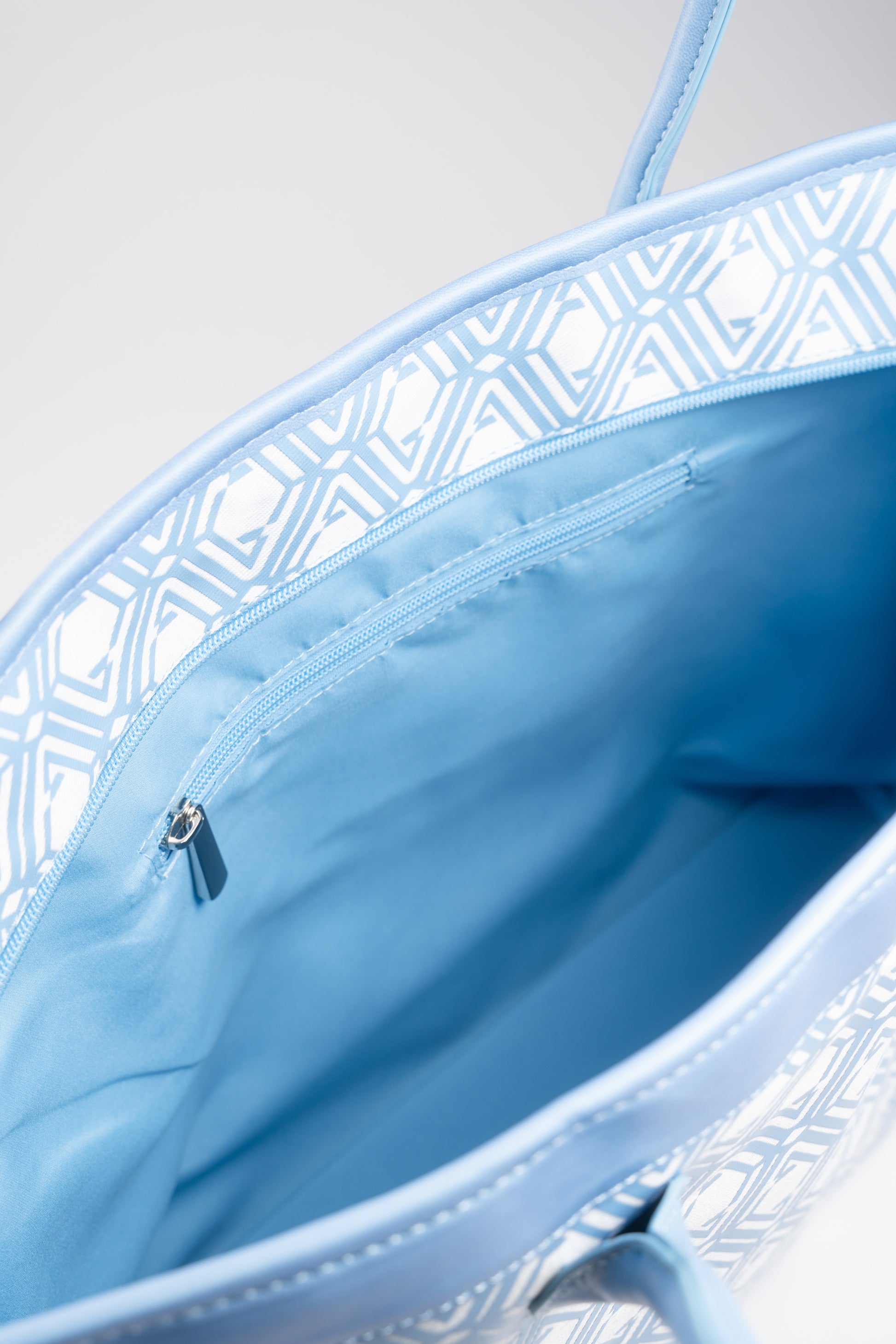 Open interior of The Monogram Bag Azure Blue showing sky-blue satin lining and zip pocket