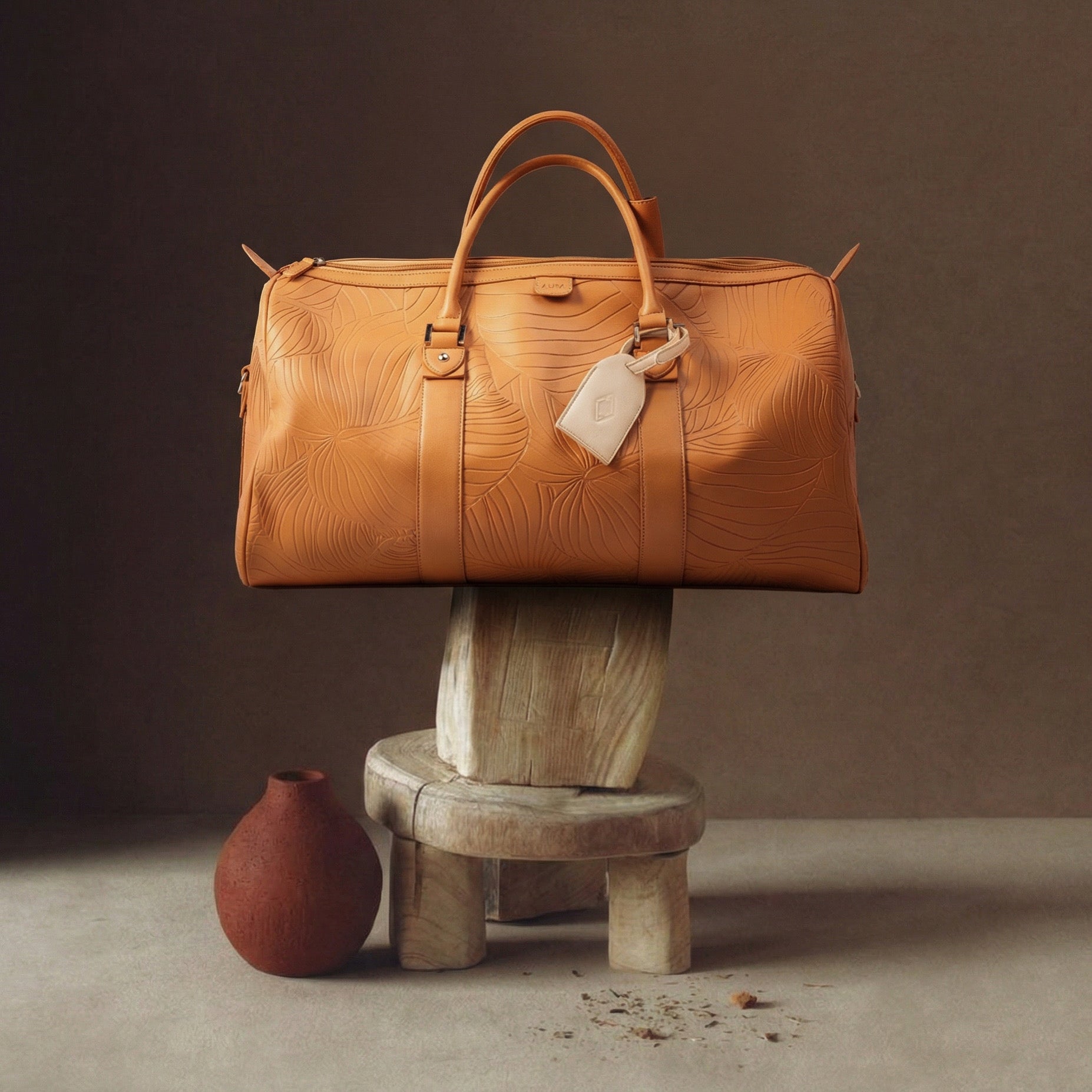 AURA Weekender Duffle in clay leaf-embossed leather styled on a wooden stool