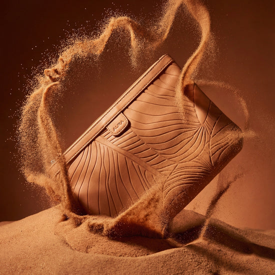 AURA Travel Pouch in Clay, leaf-embossed leather pictured on sand