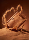 AURA Travel Pouch in Clay, leaf-embossed leather pictured on sand