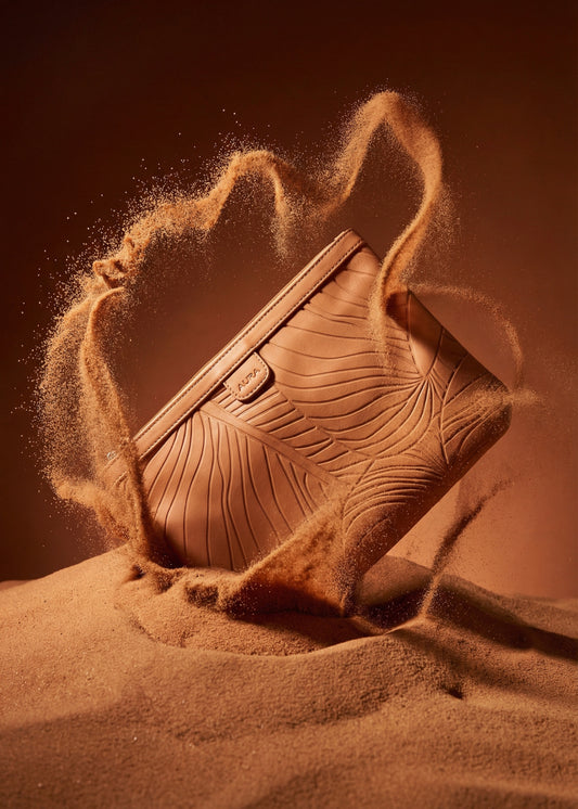 AURA Travel Pouch in Clay, leaf-embossed leather pictured on sand