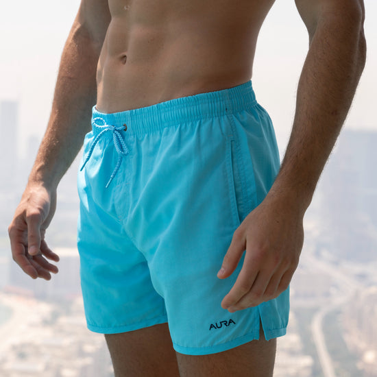 Voyager Swim Shorts in azure blue, worn against the Dubai skyline