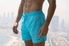 Voyager Swim Shorts in azure blue, worn against the Dubai skyline
