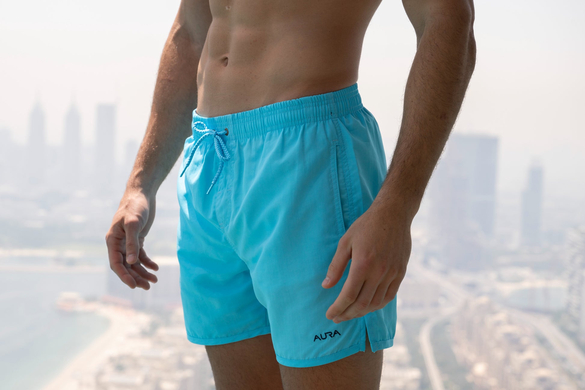Voyager Swim Shorts in azure blue, worn against the Dubai skyline