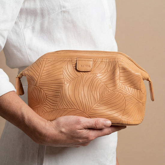 Model holding AURA wash bag in clay leaf-embossed leather