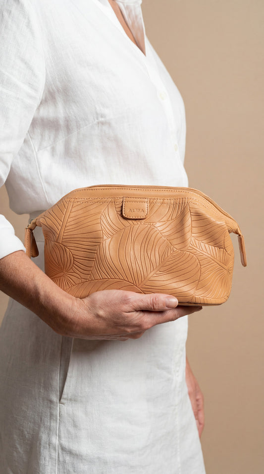 Model holding AURA wash bag in clay leaf-embossed leather