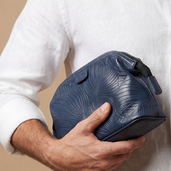 Model carrying AURA wash bag in horizon blue leaf-embossed leather